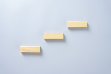 Three wooden blocks arranged as ascending steps on gray background, concept for growth, progress, business success, personal development, and achievement goal idea.