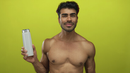 Fototapeta premium Young hispanic man holds white shampoo bottle showing bare chest in limegreen studio; confidence approval.
