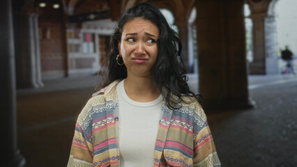 Woman face with furrowed brow and subtle frown standing under a building archway; unease uncertainty vulnerability.