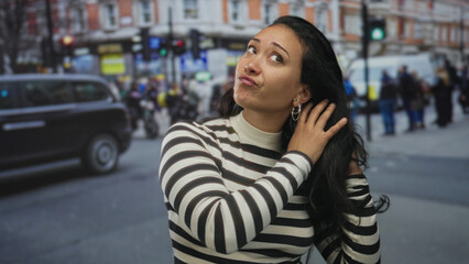 Woman touching hair with hand on busy street with pedestrians and traffic, looking skeptical and...