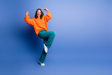 Excited Young Woman in Bright Orange Sweater Expressing Joy Against a Blue Background