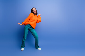 Cheerful woman in bright orange sweater on blue background enjoying autumn fashion with a casual...