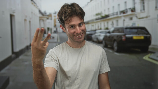 Man pointing finger and smiling on street with raised hand and casual tshirt, cars and buildings behind; playful confidence.