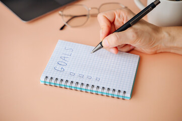 Woman writing New Year goals in notebook, planning resolutions and dreams