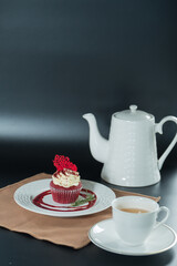A cupcake and a teapot in a elegant setting on the table