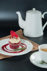 A delectable cupcake and a tea set, beautifully presented for a delightful experience. The scene features a cupcake with red velvet, a teapot, a teacup, and a decorative plate.