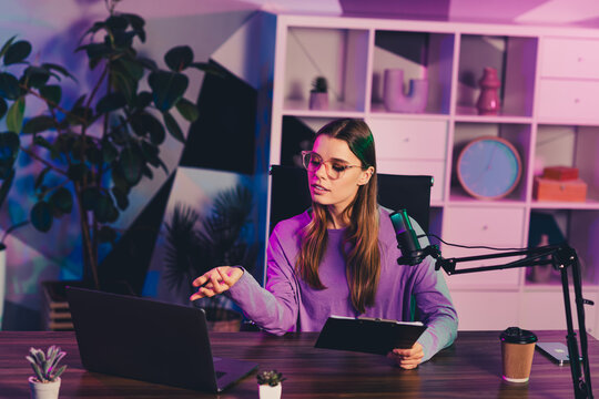 Young woman creating a podcast in a modern home studio with vibrant lighting using a microphone and laptop