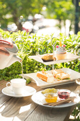 Afternoon tea, with a tiered tray of desserts and a cup being filled with tea. A perfect treat for a relaxing moment!