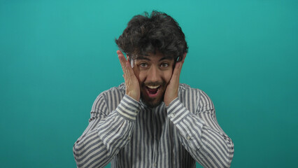 Hispanic man with beard expressing surprise and joy against a blue background, wearing striped...