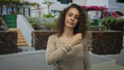 Woman checking wristwatch while looking down near stone building steps on a sunny street; thoughtful pause.
