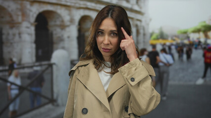 Woman gesturing in a beige coat outside the iconic roman colosseum in italy, conveying curiosity...