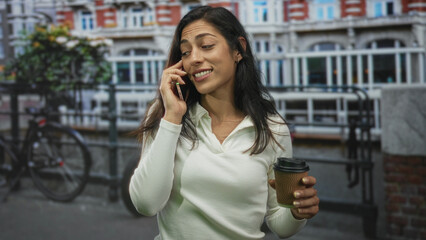 Woman talking on phone holding takeaway coffee cup on an amsterdam street; easy casual chat contentment.