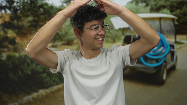 Man smiles broadly and raises bare arms overhead forming a triangular frame under forest canopy; hope joy.
