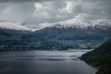 Obraz premium Snow-capped mountains and clouds surround a serene town by the norwegian fjord.