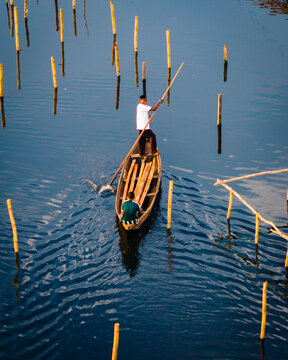 Aerial view of a man navigating a wooden boat through a watery landscape dotted with wooden posts, rippling reflections creating a mesmerizing dance of light, Lagos, Lagos, Nigeria.