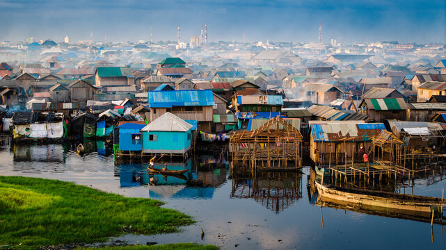 Aerial view of stilt houses creating a vibrant tapestry of blues and browns over the water, reflecting the hazy sky, Lagos, Lagos, Nigeria.