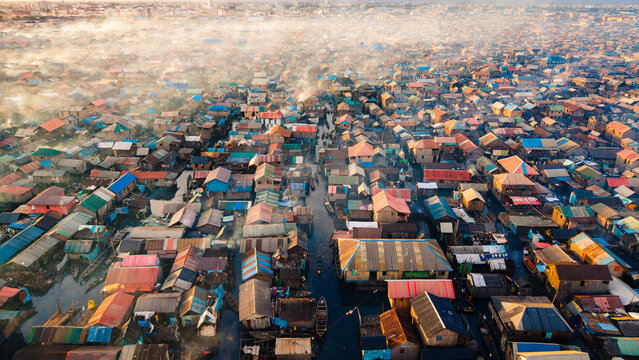 Aerial view of a sprawling settlement with dense rooftops and waterways, a vibrant tapestry under a soft, smoky haze, Lagos, Lagos, Nigeria.