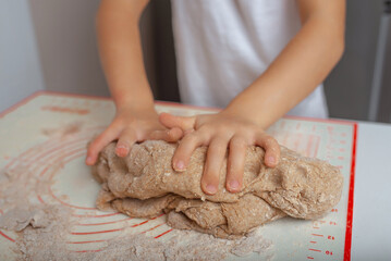 A child kneads dough on a silicone baking mat.