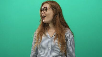 Woman standing smiling with open mouth wearing glasses and a striped shirt in bright green studio;...