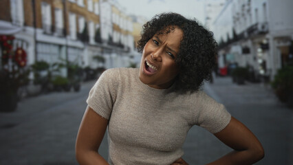 Young woman clutching stomach with furrowed brow and pursed lips on busy pedestrian street;...