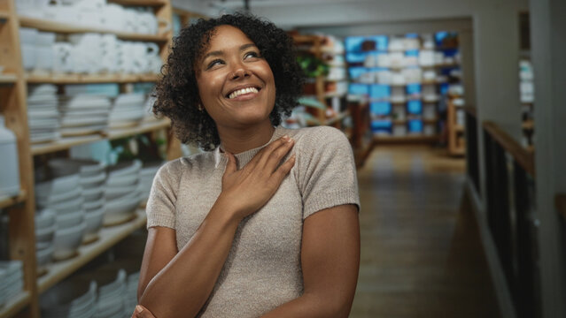 African american woman with hand on chest and brushing hair near colorful decor shelves in building; gratitude.