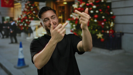 Young man with beard making rude gesture outdoors near holiday decorations on city street with festive background and casual attire suggesting urban cheer and youth expression