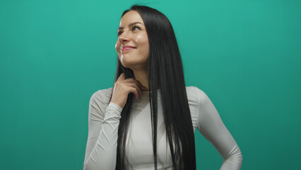Woman smiling confidently wearing white against a vibrant green background, exuding positivity and calmness with long dark hair framing her face effortlessly.