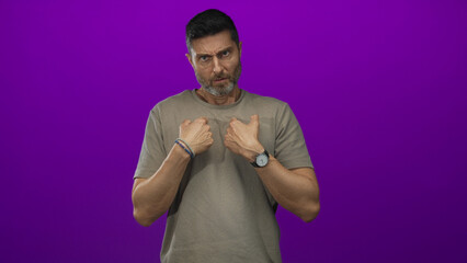 Hispanic man points fingers to chest showing hands and wristwatch in purple studio; confusion doubt.