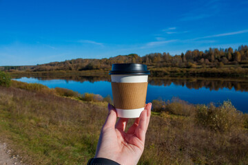 Hand Holding Takeaway Coffee Cup Against Autumn River Daugava Landscape