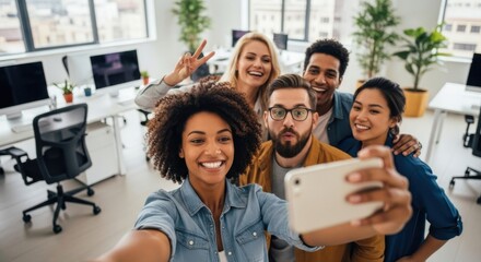 Happy diverse business team taking a selfie in a modern office. Young multiracial colleagues enjoy work friendship, collaboration, and fun. Teamwork, unity, positive corporate culture.