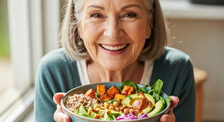 Happy senior woman showing a healthy vegan Buddha bowl. Smiling mature lady with nutritious lunch of quinoa and avocado. Healthy lifestyle, diet, and wellness concept.