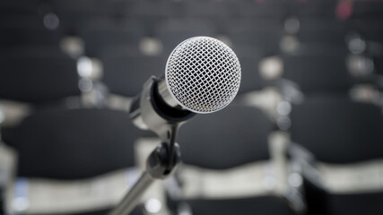 Close-up view of a professional microphone on a stand with empty chairs in the background,...