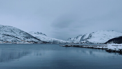 Snow-covered mountain slopes tower above the water. It's a cloudy day. Norway
