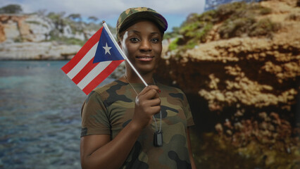 African american soldier holding puerto rico flag in camouflage uniform cap and dogtags by seaside cliffs; pride.