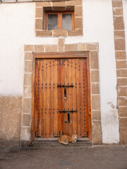 An orange cat rests peacefully on the doorstep of a traditional studded wooden door in Essaouira, Morocco, beneath a rustic window.