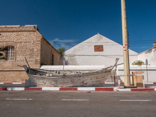 Historic Essaouira Street Scene: An Old Wooden Boat Resting on the Curb Against Traditional Moroccan Architecture Under a Clear Sky