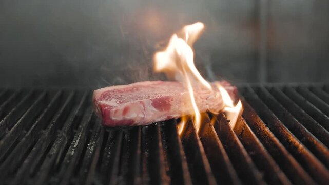 A raw steak sizzles on a grill as open flames rise beneath it, capturing the intensity and flavor or live-fire cooking.
