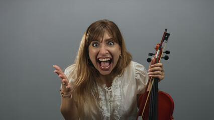 Woman holding violin and bow with open mouth shouting pose in gray studio wearing white blouse; raw excitement.