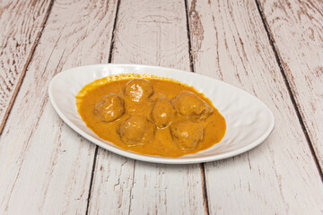 Cod meatballs in a green sauce with clams, garnished with chili pepper and served in a clay pot with toasted bread