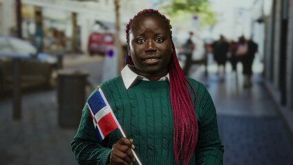 Fototapeta premium Woman holding dominican republic flag outdoors in city street, expressing emotions in vibrant urban scene with diverse background showcasing cultural pride.