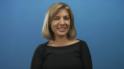 Woman face smiling in a blue studio wearing a black top and casual hair parted bob style portrait;...