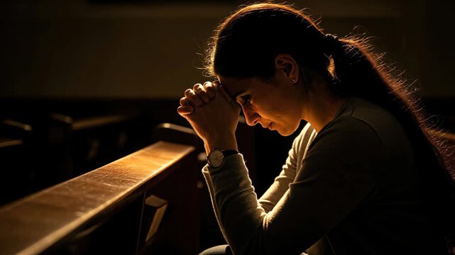Christian woman praying alone on his knees in church with warm light representing faith and hope.