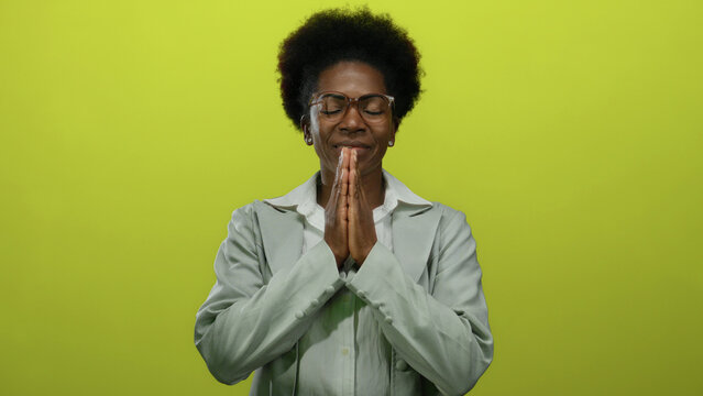 Woman smiling in prayer pose over isolated yellow background emphasizes peace, relaxation, spirituality, positivity, and mindfulness, embodying youthful tranquility and focus.