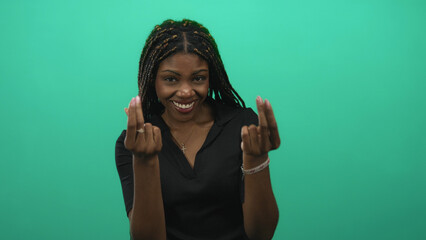 Woman with pinched fingers gesture and sly smile in green studio wearing black polo top and gold...