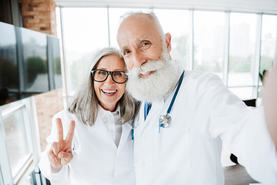 Funny doctor duo selfie in bright clinic with senior couple of physicians smiling and posing for a friendly health care moment