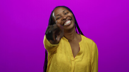 Woman smiling in yellow blouse pointing directly at camera with vibrant purple background, conveying positivity and engagement with focus on her expressive gesture and lively setting.