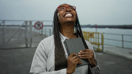 Woman smiling with tablet on promenade beside sea showcasing happiness connectivity and technology
