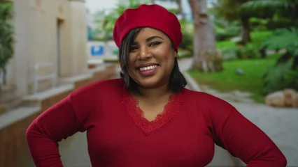 Fototapete Rund Bordeaux Woman smiling outdoors in a vibrant red outfit and beret on a city street surrounded by greenery and buildings with a cheerful expression embodying confidence and style.  © Krakenimages.com
