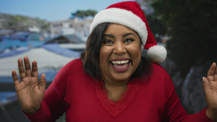 Woman in red sweater and santa hat smiling joyfully outdoors with a scenic blurry background in a...