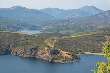 Fototapeta premium Panoramic view from an elevated viewpoint showing the contrast between the deep blue of the reservoir and the vibrant green of the mountains